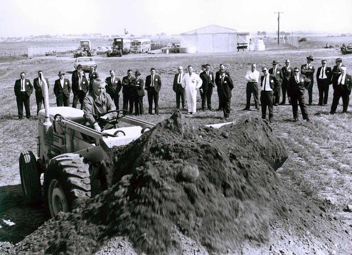Group of men standing in field watching equipment display.