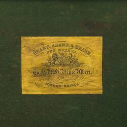 Yellow label with ornately decorated printing featuring coat of arms and and cursive text.