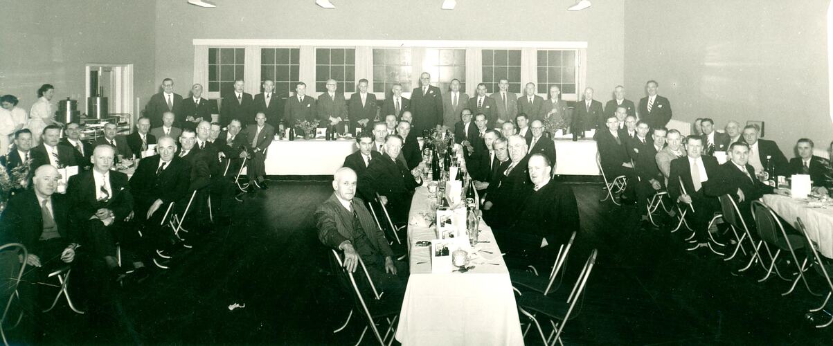 Large group of men sitting and standing at tables.