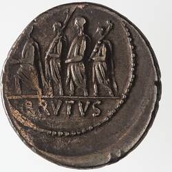 Round coin, aged, four figures walking to the left, carrying sticks.