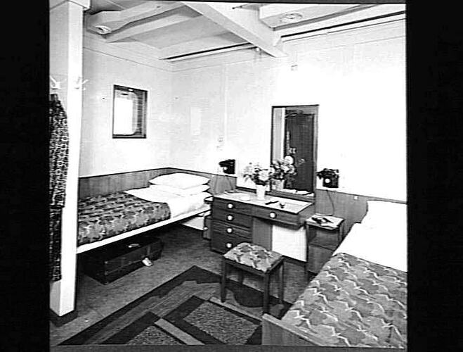 Ship interior. Two single beds, one against wall. Dressing table and stool in between.