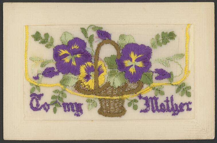 Card with embroidered basket containing purple and yellow flowers with green foliage. Purple lettering at base