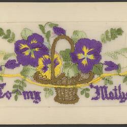 Card with embroidered basket containing purple and yellow flowers with green foliage. Purple lettering at base