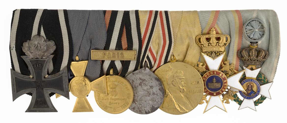 Group of seven medals with ribbons joined together in a row.