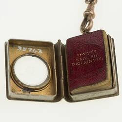 Detail of silver watch chain with miniature red book in silver case with cut-out circle. Case open.