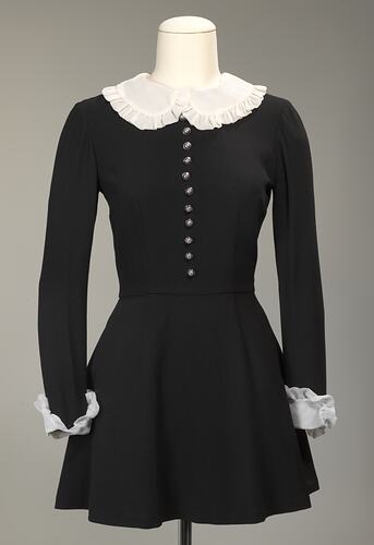Long sleeved black wool mini dress. White collar and cuffs. Silver buttons down front.