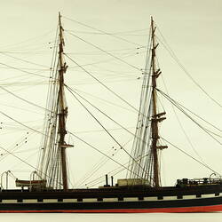 Side view of three masted ship with red hull.
