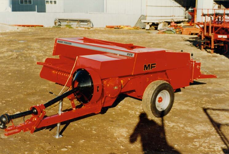 Colour photograph of a Pickup Baler in a dirt ground near building.