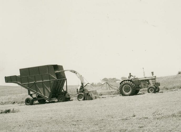Man driving a tractor towing a forage harvester and transport bin.
