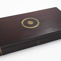 Wooden case with circular brass inlay on lid. Brass hinges.