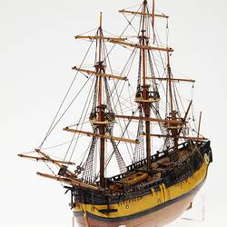 Wooden ship model with varnished hull, yellow and black painted quarters and rudder, and three masts with rigg