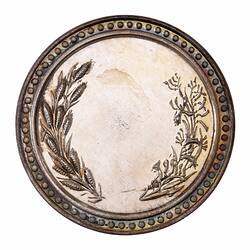 Round medal with blank section in centre framed by wheat and native flora. Decorative edge.