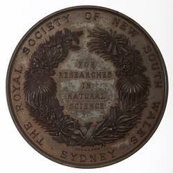 Medal with text framed by wreath. Text around wreath.