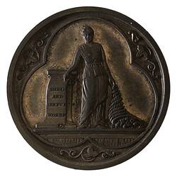 Round bronze medal with trefoil housing figure of Plenty. She points to words on a scroll.