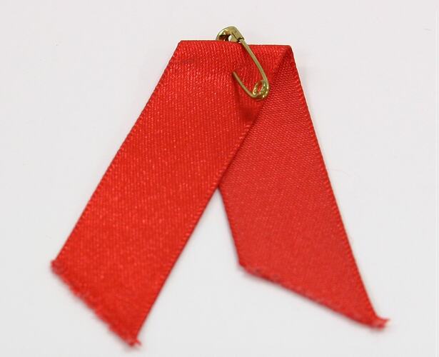 Folded red ribbon with gold pin at top.