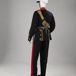 Back of navy officer's uniform with gold at cuff, sash, epaulettes, belt. Red/gold collar. White helmet.