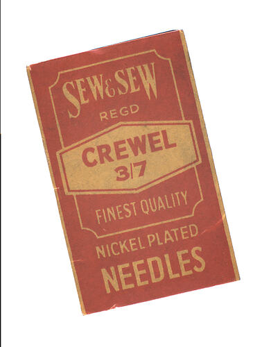 Red and yellow needlebook containing 9 nickel-plated needles fastened onto a sheet of gauze.