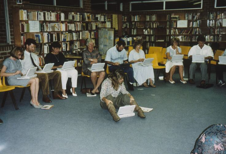 A group of teachers sitting in a row in a library looking at laptops.