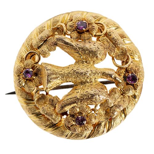Round gold brooch with large bird and four purple paste stones.