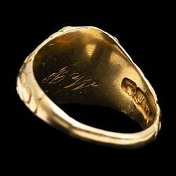 Back view of large gold ring. Internal side of ring has stamp and engraved letters.