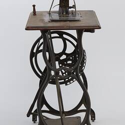 Sewing machine fitted to a metal frame with a wooden bench.