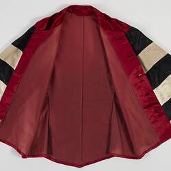 Red riding jacket with red buttons. Black and white hoops on sleeves. Short stand up red collar. Flat/open.