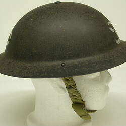 Metal helmet with green chin strap on white mannequin head.