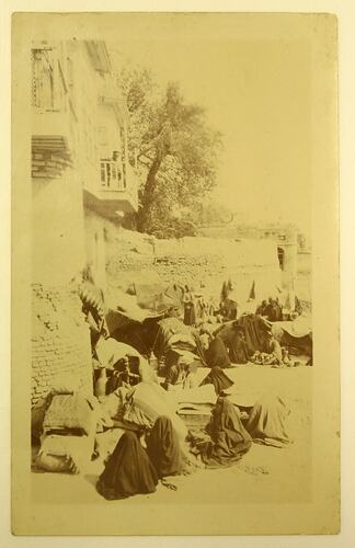 Crowd of Arab women and some men, seated next to wall.