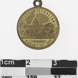 Round gold coloured medal with building and text above and below.