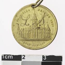 Round gold coloured medal with building, text surrounding.