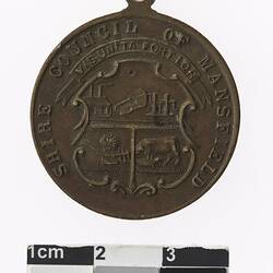 Round medal with coat of arms, text surrounding.