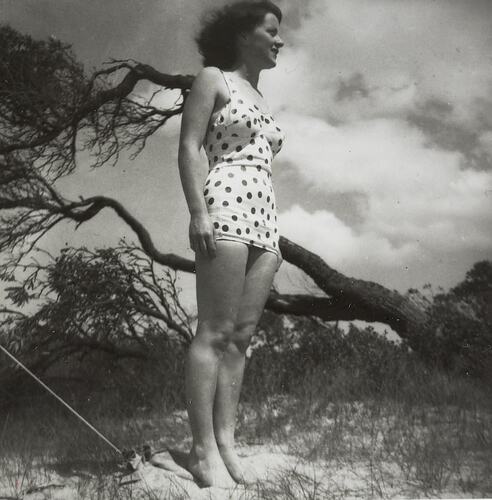 Woman in spotted bathers by tree on sand.
