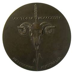 Round bronze medal with ram head skull and text.