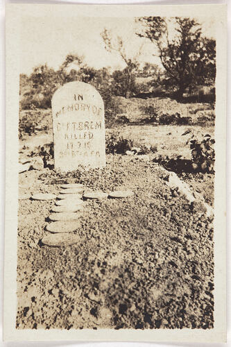 Grave with inscribed headstone, on ground before grave is cross shape made from circular shapes.