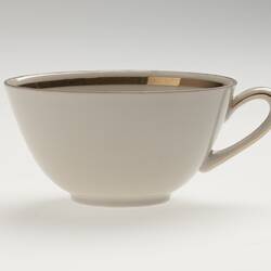 Delicate white china cup with a gold metallic band around the inside rim and on the handle.