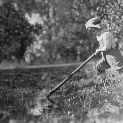 Boy pushing down on a long pole into water from the bank.