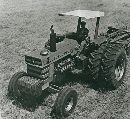 Man driving a tractor fitted with dual rear wheels and coupled to a disc plough.