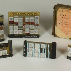 Five integrated circuit boards, with chips, LEDs and resistors soldered on, and one cardboard box with a punch