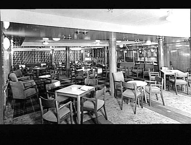 Ship interior. Lounge area with wooden chairs around tables.