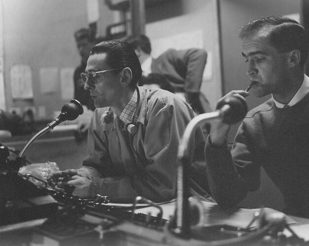 Two male television production staff sitting at a control panel in a television studio.