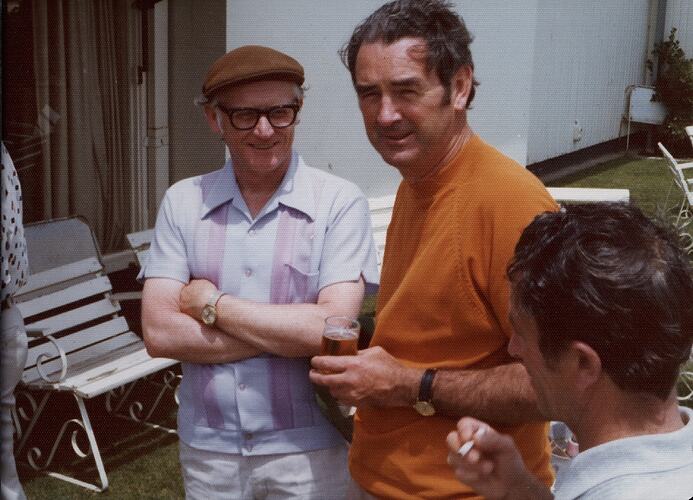 Three men outside drinking, smoking and talking.