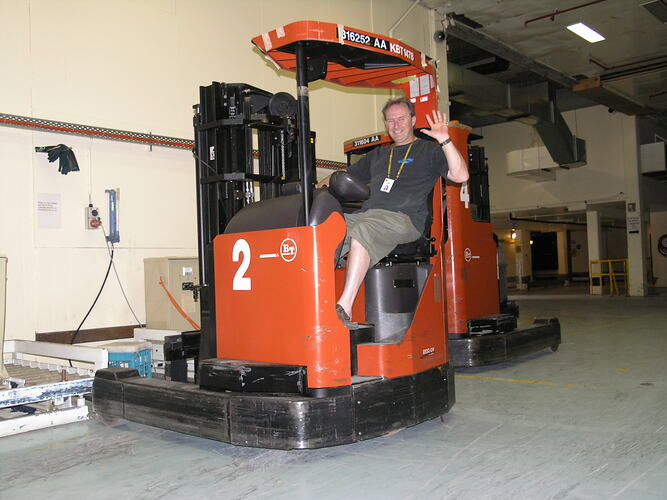 Man on forklift, waving to camera.