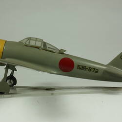 Green grey plane model with red spot on each wing and fusleage. Yellow nose, black propeller. Profile.