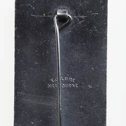 Back of rectangular cast metal badge. Vertical pin attached and suspension loop at top.