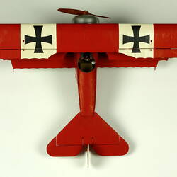 Red aeroplane model. White strip on top of wings with black cross. Aerial view.