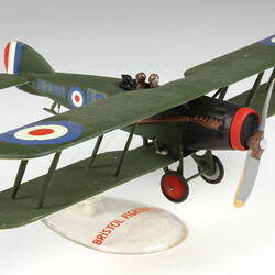 Dark green aeroplane model with red, white, blue circles on clear stand. Three quarter view.
